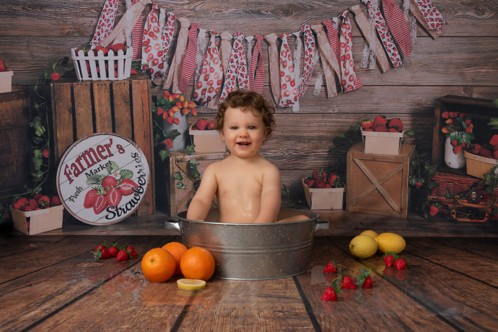 Bébé dans une bassine en fer, entouré d'oranges, citrons et fraises