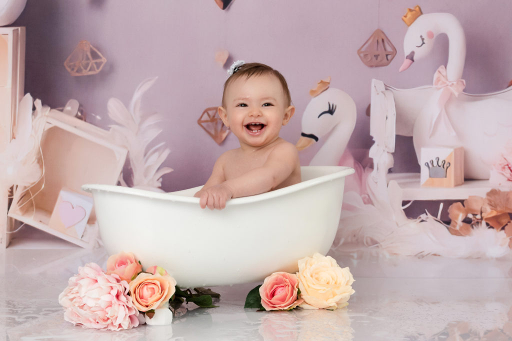 Petite fille dans une baignoire devant un décor rose avec des cygnes et fleurs