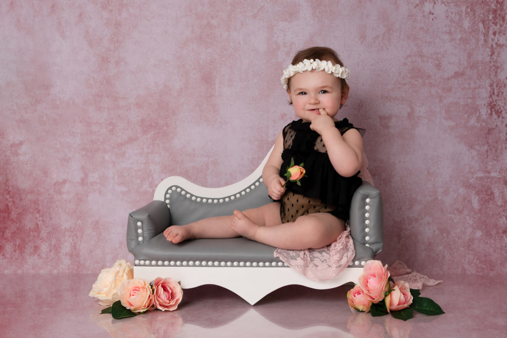 Jolie petite fille sur une méridienne grise devant un mur texturé rose