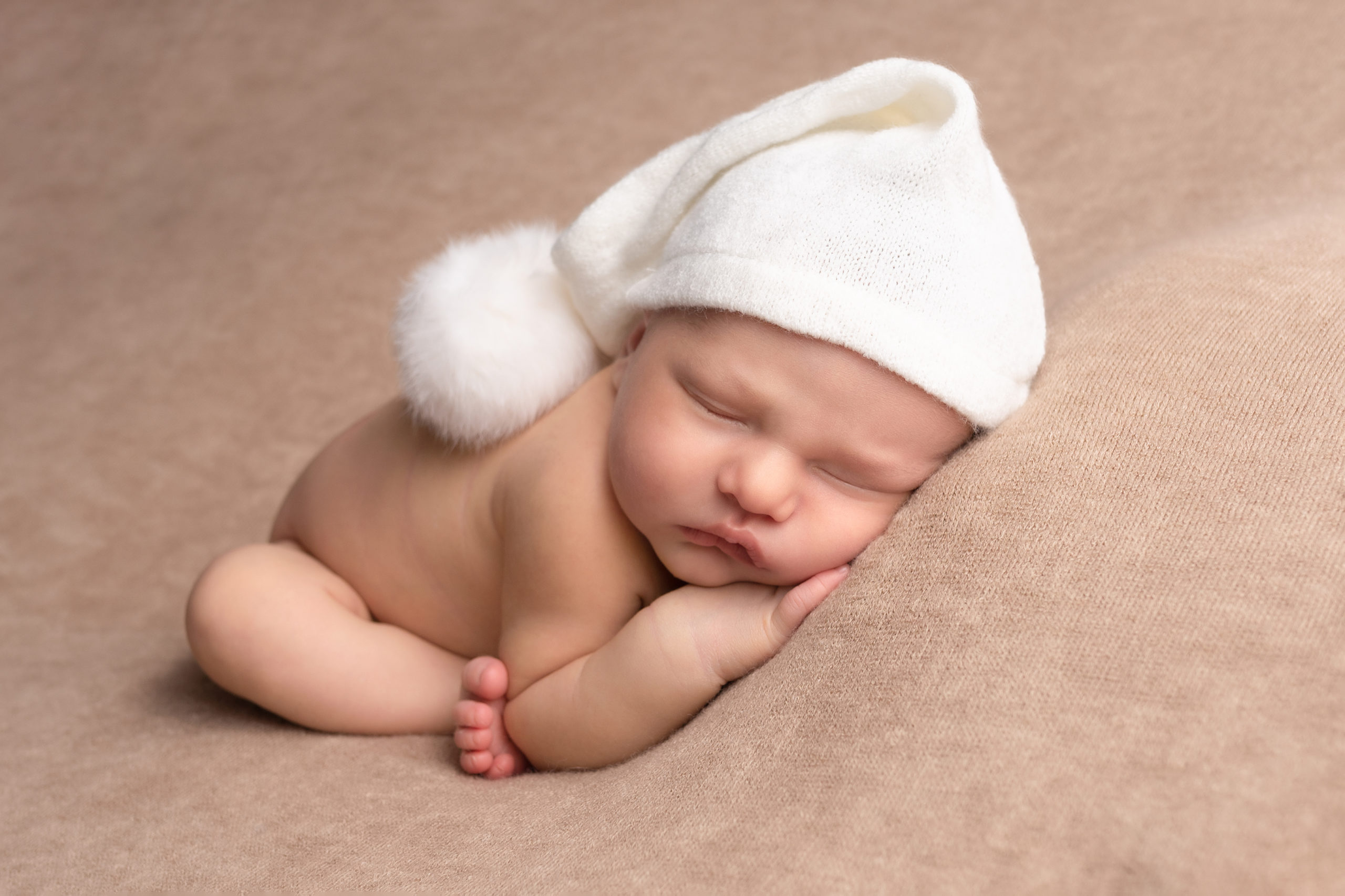 Nouveau-né couché sur le ventre avec un bonnet à pompon blanc