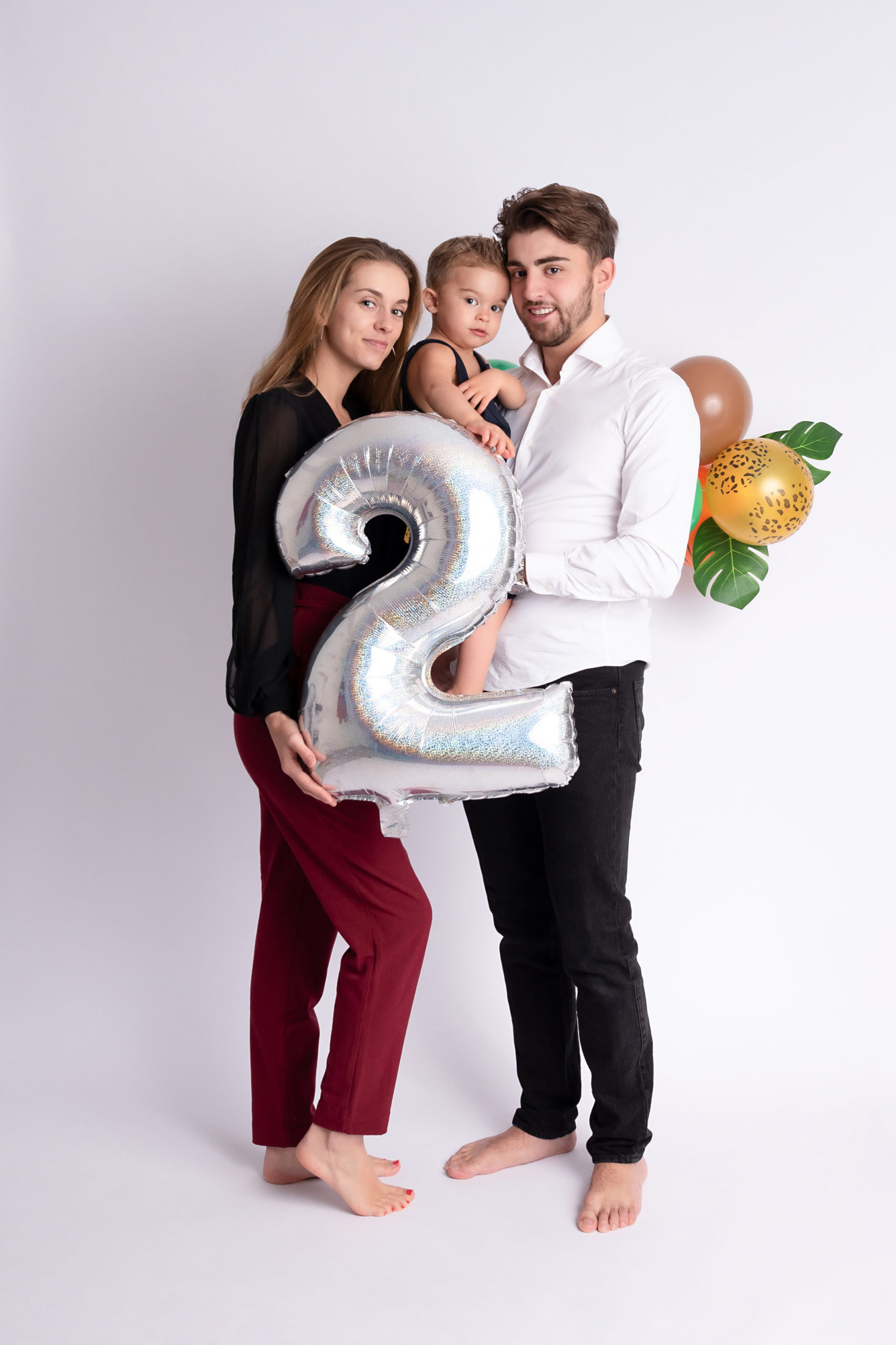 Jeunes parents qui portent sur fils dans les bras et un ballon en forme de chiffre deux pour son anniversaire