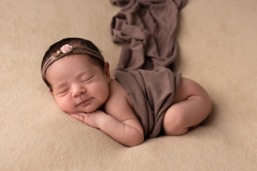 Bebe fille sur une couverture beige, avec un petit bandeau marron