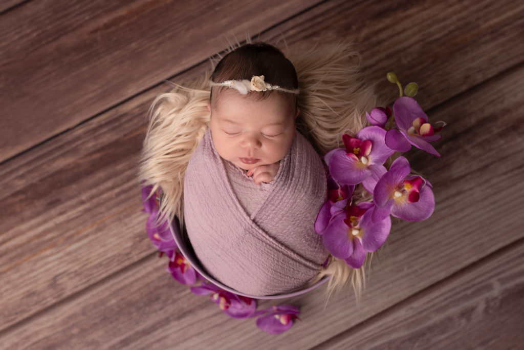 bébé dans un seau violet, entouré d'orchidées