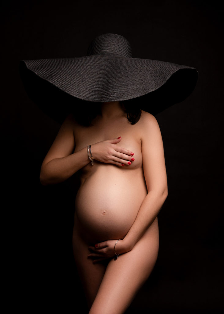 Femme enceinte nue avec un grand chapeau noir qui lui cache le visage